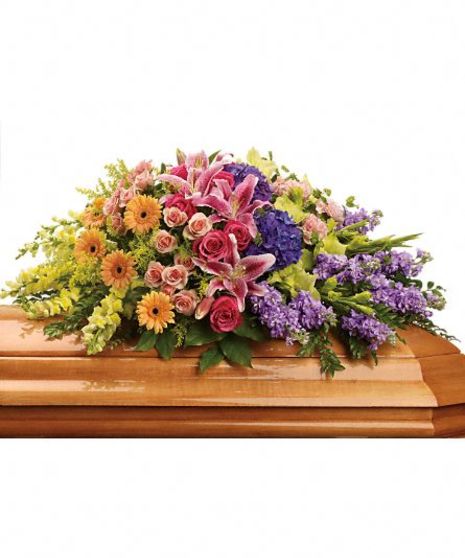 Rainbow casket spray of pink, orange, purple and green flowers with greenery.